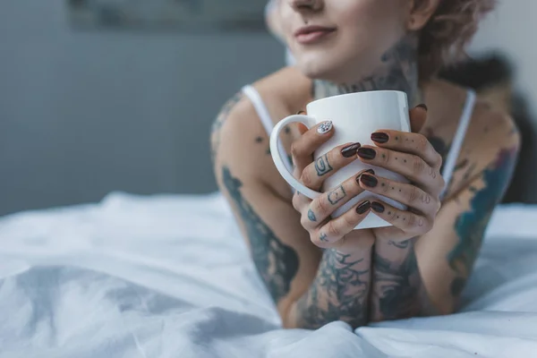 Vista cortada de menina tatuada bebendo café na cama de manhã — Fotografia de Stock