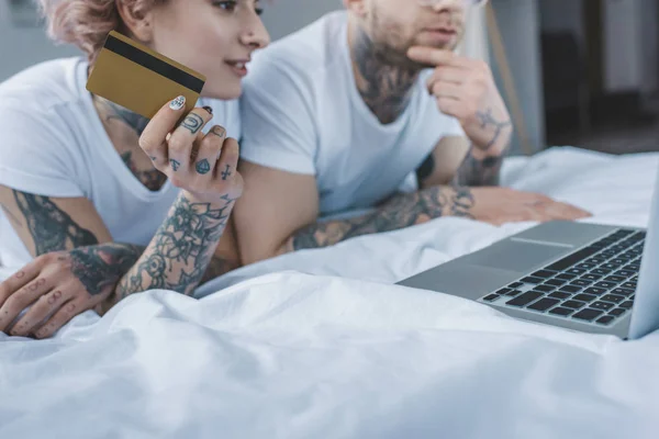 Junges tätowiertes Paar shoppt online mit Kreditkarte und Laptop im Bett — Stockfoto