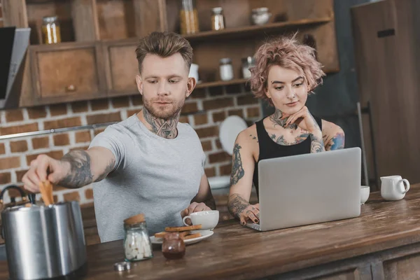 Young tattooed couple using laptop during breakfast in kitchen — Stock Photo