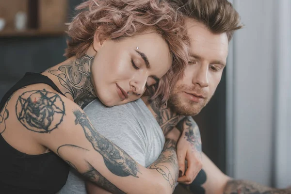 Joven pareja tatuada abrazándose con los ojos cerrados - foto de stock