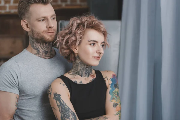 Jovem tatuado casal abraçando e olhando para longe — Fotografia de Stock