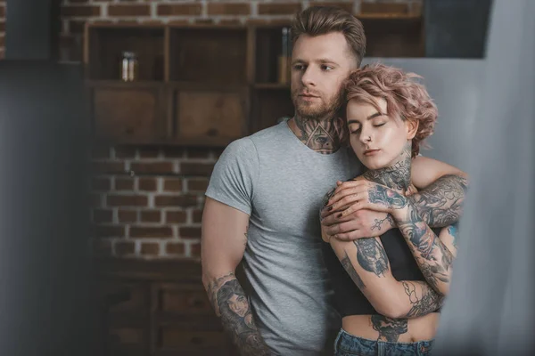 Tierna pareja tatuada abrazándose en la cocina - foto de stock