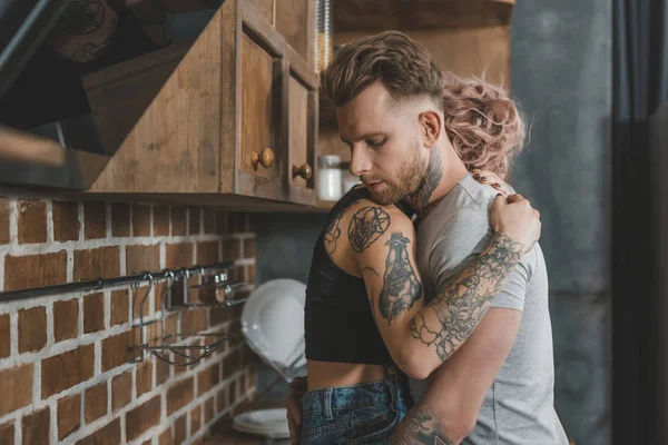 Jovem tatuado casal abraçando na cozinha — Fotografia de Stock