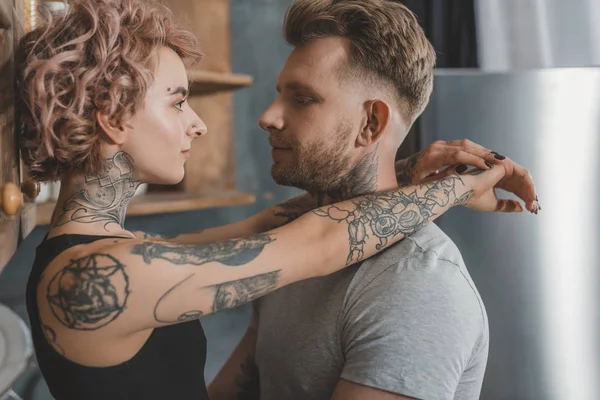 Pareja tatuada abrazándose y mirándose - foto de stock