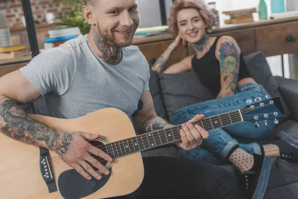 Namorado tocando na guitarra acústica para sua namorada em casa — Fotografia de Stock