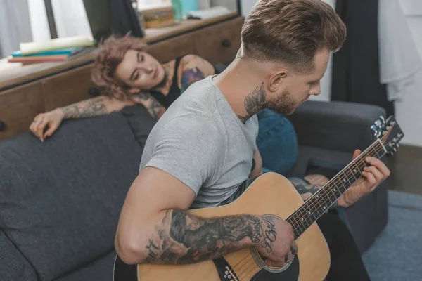 Boyfriend playing on acoustic guitar for his girlfriend at home — Stock Photo