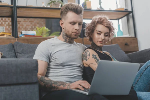 Attraktives tätowiertes Paar mit Laptop auf dem heimischen Sofa — Stockfoto
