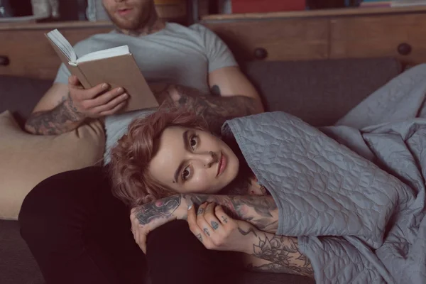 Couple tatoué relaxant et livre de lecture à la maison — Photo de stock