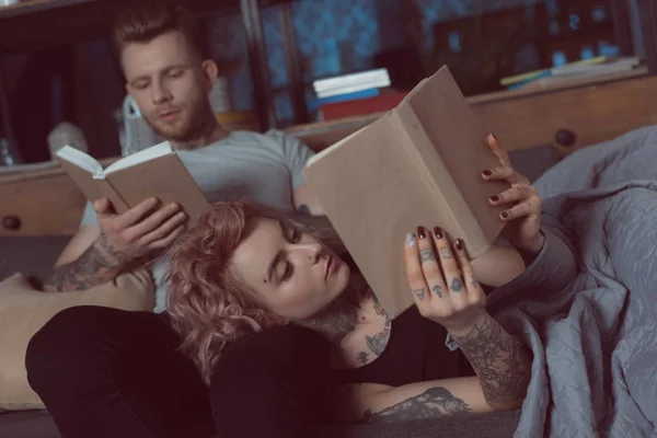 Tatuado casal relaxante e leitura de livros em casa — Fotografia de Stock