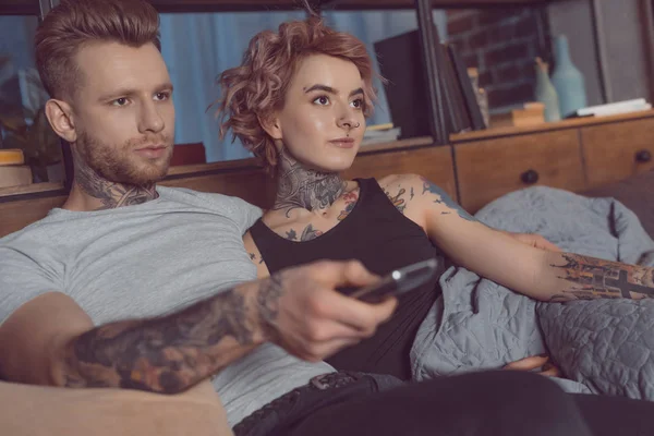 Tattooed couple with remote controller watching tv at home — Stock Photo