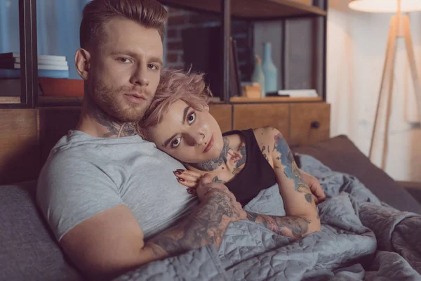 Belo casal tatuado relaxante na cama em casa — Fotografia de Stock