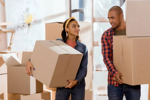 Pareja afroamericana sosteniendo cajas de cartón y mudándose a nuevo apartamento - foto de stock
