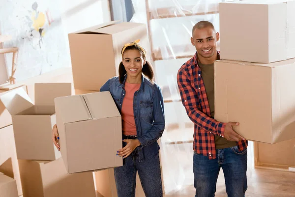 Hermosa pareja afroamericana sosteniendo cajas de cartón y mudarse a un nuevo hogar - foto de stock