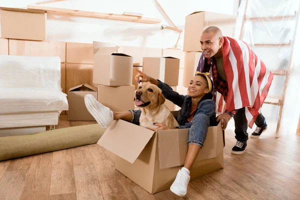 African american couple having fun with dog in new apartment — Stock Photo