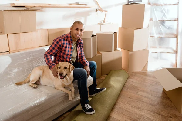 Homem americano africano com cão labrador em novo apartamento com caixas de papelão — Fotografia de Stock