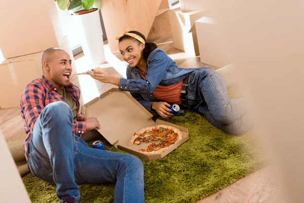 Coppia afroamericana mangiare pizza nel nuovo appartamento con scatole di cartone — Foto stock