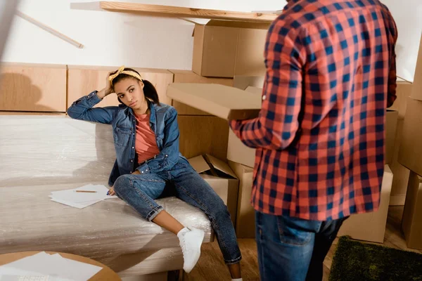 Втомилася афроамериканська дівчина дивиться на свого хлопця з піцою, переїжджаючи в нову квартиру — стокове фото