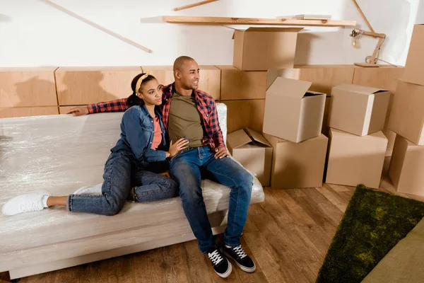Pareja afroamericana soñadora en apartamento nuevo con cajas de cartón - foto de stock