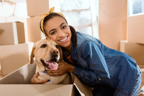 Sorridente mulher americana africana com cão labrador em caixa de papelão — Fotografia de Stock