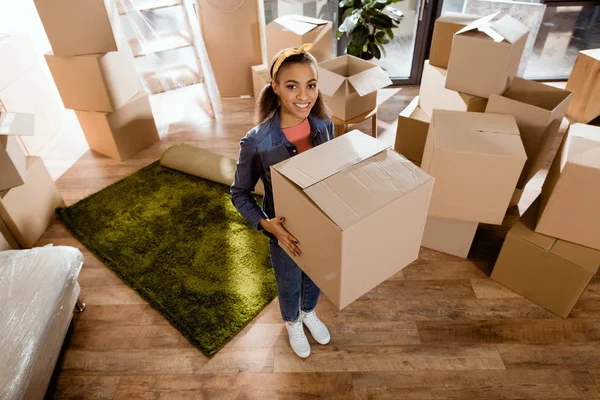 Jovem sorridente menina americana africana segurando caixa de papelão e se mudando para uma nova casa — Fotografia de Stock