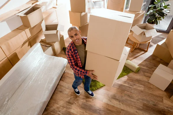 Young african american man holding cardboard box and moving into new home — Stock Photo