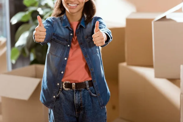 Recortado vista de atractivo afroamericano chica con los pulgares hacia arriba en nuevo hogar - foto de stock