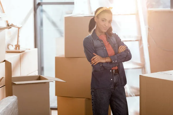 Attractive african american girl posing in new home with cardboard boxes — Stock Photo