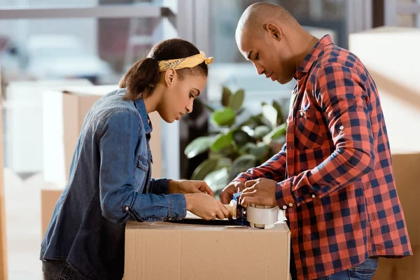 Caja de cartón de embalaje de pareja afroamericana con cinta adhesiva - foto de stock