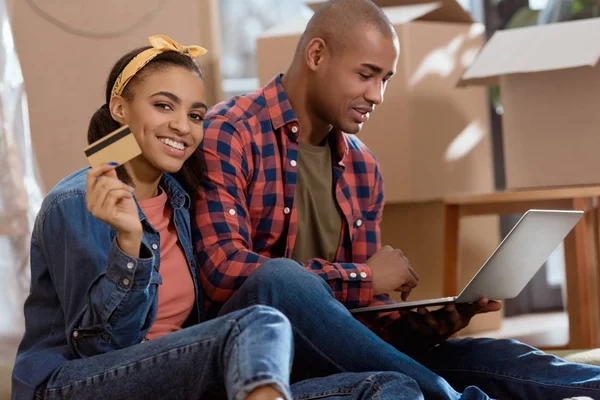 Africano americano pareja compras en línea con tarjeta de crédito y portátil en nuevo apartamento - foto de stock