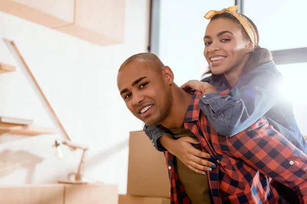 Feliz africano americano pareja piggybacking en nuevo hogar - foto de stock