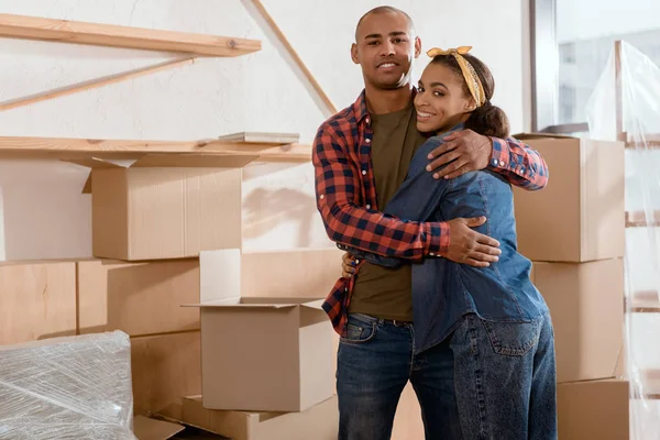 Heureux couple afro-américain câlin dans un nouvel appartement avec des boîtes en carton — Photo de stock