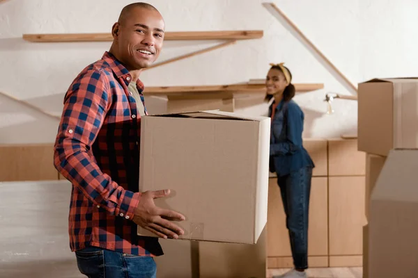 Heureux couple afro-américain tenant boîte en carton et déménageant dans un nouvel appartement — Photo de stock