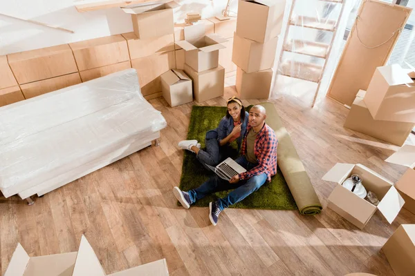 African american couple using laptop in new home with cardboard boxes — Stock Photo