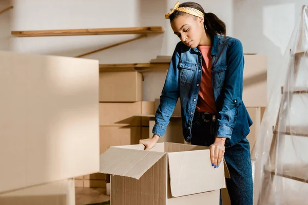 Disgustada chica afroamericana desempacando cajas de cartón en nuevo apartamento - foto de stock