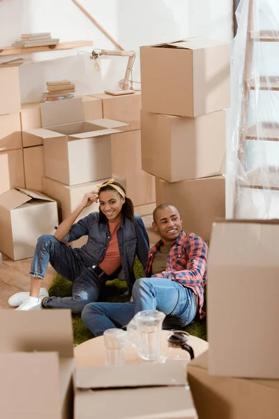 Африканская американская пара отдыхает на полу в новом доме с картонными коробками — стоковое фото