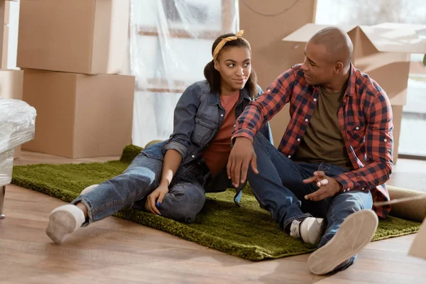 Africano casal americano sentado no chão em novo apartamento com caixas de papelão — Fotografia de Stock