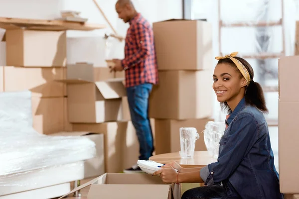 Smiling african american girl unpacking dishware in new home — Stock Photo