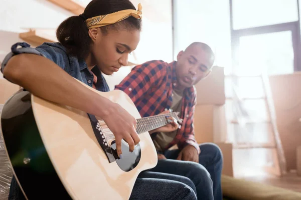 Afroamericana novia jugando en acústica guitarra para novio en nuevo apartamento - foto de stock