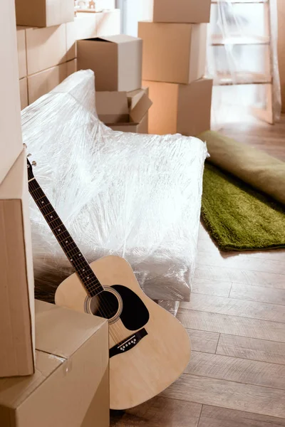 Sofa, acoustic guitar, rolled carpet and cardboard boxes in new home — Stock Photo