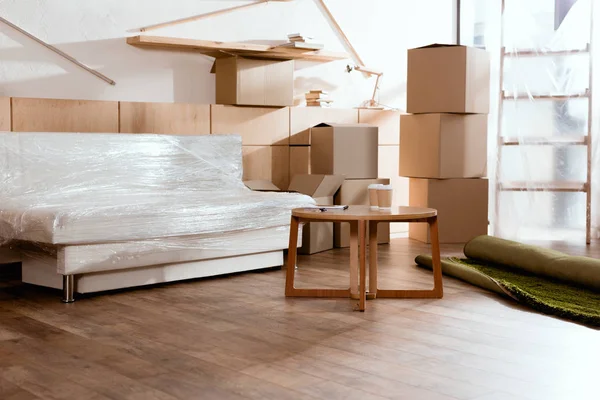 Sofa, table, rolled carpet and cardboard boxes in new apartment — Stock Photo