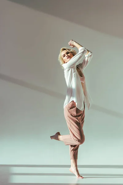 Vista completa di bella donna a piedi nudi in reggiseno rosa, camicia e pantaloni in posa in studio — Foto stock