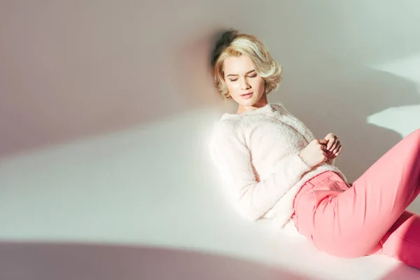 Beautiful blonde girl in pink clothes lying in studio on grey — Stock Photo