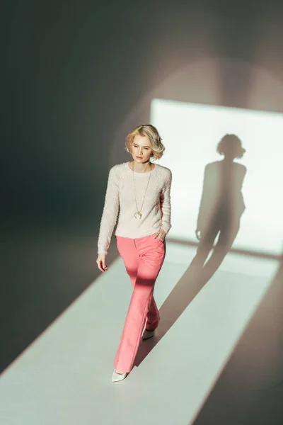 Высокий угол зрения красивой блондинки в трикотажном розовом платье, идущей в студии — стоковое фото