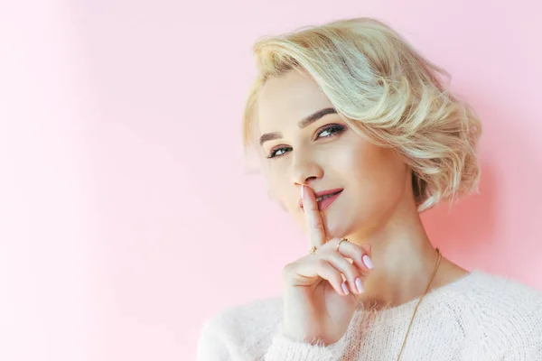 Hermosa chica rubia haciendo un gesto de silencio y mirando a la cámara aislada en rosa - foto de stock