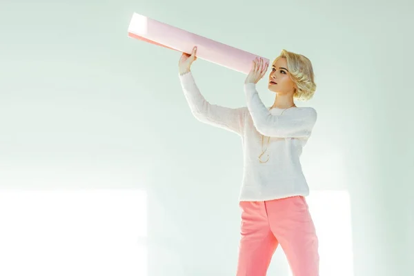 Bela mulher bonita olhando através de papel rosa rolado em estúdio — Fotografia de Stock