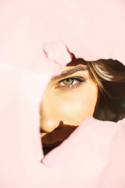 Красивая девушка смотрит на камеру сквозь порванную розовую бумагу — стоковое фото