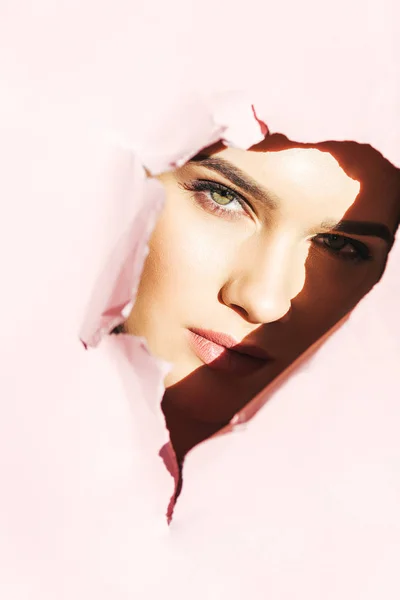Attractive girl looking at camera through torn pink paper — Stock Photo
