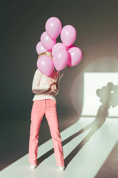 Вид в полный рост стильной молодой женщины, позирующей с розовыми воздушными шарами в студии — стоковое фото