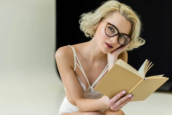 Красивая девушка в кружевном белье и очки для чтения книги — стоковое фото