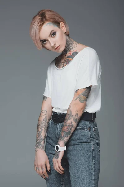 Portrait of beautiful girl with tattoos wearing white t-shirt and looking at camera isolated on grey — Stock Photo